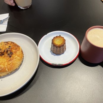 Cellar Door Cafe - (From left to right) Za'atar, cheese, and onion bialy, canelé, and spiced butterscotch apple cider - American Near Me - Lawrence, Kansas