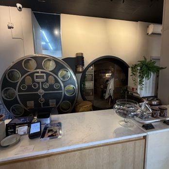 Vesta Chocolate - Interior - A marble counter features a large film reel prop and a glass bowl, with a circular doorway and some plants in the background. - Coffee & Tea Near Me - Upper Montclair, New Jersey