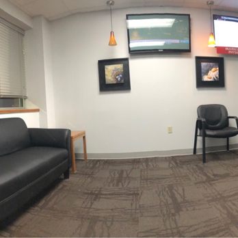 Physicians Immediate Care - Waiting lobby - A waiting room features black leather sofas, chairs, a window with blinds, and wall-mounted TVs, with a reception desk visible in the background. - Urgent Care Near Me - Aurora, Illinois