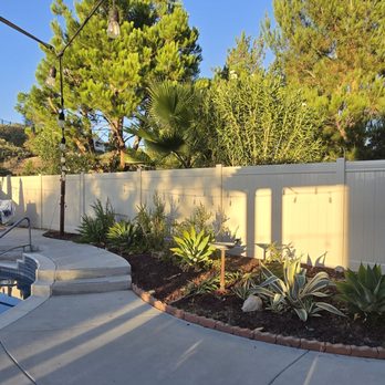 Ergeon - A backyard features a swimming pool with a concrete patio, garden beds with succulents, and a white privacy fence, with trees and string lights overhead. - Fences & Gates Near Me - Riverside, California