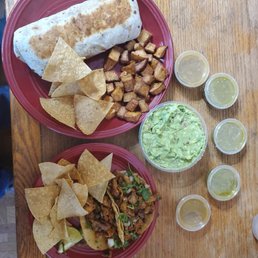 Breakfast Burrito and potatoes with some chips at the top and 2 El Pastor tacos and some chips at the bottom. Fresh guacamole between the 2