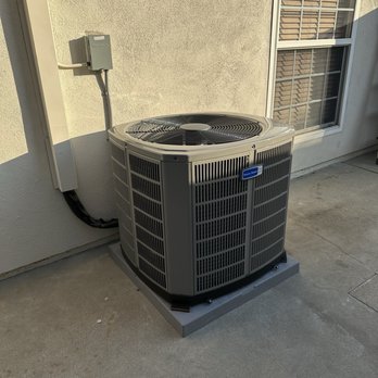 Evolution Heating And Air Conditioning - 3 ton American Standard Silver AC compressor - A gray American Standard outdoor air conditioning unit is positioned on a concrete pad next to a building wall with a window, connected to electrical wiring. - Heating & Air Conditioning/HVAC Near Me - Fullerton, California