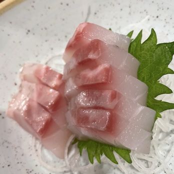 Mikuni - Raw fish sashimi slices are arranged on a speckled ceramic plate with a green leaf and shredded daikon radish for garnish. - Japanese Near Me - Davis, California