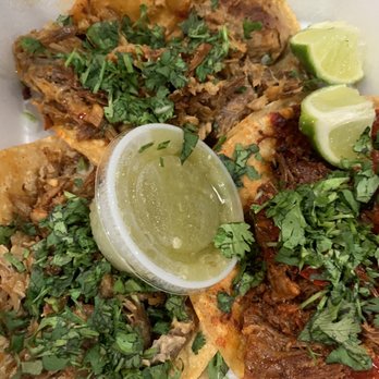 El Compa - Three tacos filled with shredded meat, topped with chopped cilantro, served with lime wedges on a white plate. The tacos have different fillings, with one appearing to have a red sauce and another with a more shredded meat filling. The lime wedges are cut into small pieces and placed on top of the tacos for added flavor. - Mexican Near Me - Birmingham, Alabama