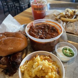 Brisket Sandwich - The image shows a meal at City Barbeque with a brisket sandwich, baked beans, fries, and a soda on a tray in a restaurant setting.