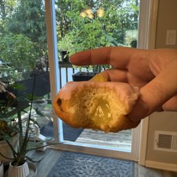 Strawberry lemon donut - A hand holds a donut with pink glaze and lemon filling, with a background of a glass door and green plants outside.