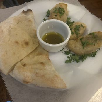 Bar Camillo - Zucchini - A plate contains a piece of naan bread and three fried dumplings garnished with chopped herbs. A small white cup of green sauce or oil is placed in the center. The dish is served on white paper, likely in a restaurant setting, with a wooden surface visible in the background. - Italian Near Me - Brooklyn, New York