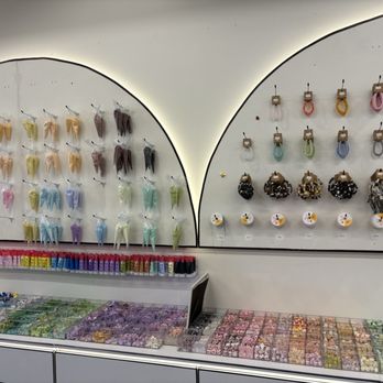 2D DIY Studio - The image shows a retail store display with hair accessories. On the wall, there are multiple scrunchies in different colors and patterns hanging on hooks, organized in rows. Below, there are containers filled with small hair accessories such as beads and decorative items. The display is neatly arranged, with a clean, modern aesthetic, and the accessories are colorful and varied, suitable for personal styling or gift purposes. - Art Classes Near Me - Troy, Michigan