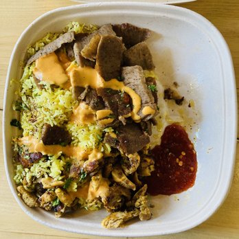 Rumi Middle Eastern Grill - $8 Meat Lunch Special (w/ rice, gyro meat, chicken shwerma, spicy tahini sauce and hot sauce). Not pictured: the lentil soup. - A takeout container contains Middle Eastern cuisine with yellow rice topped with herbs, slices of gyro meat, and pieces of cooked meat. There are drizzles of spicy tahini sauce and hot sauce on the food. The container is placed on a wooden surface, and the food appears freshly prepared and served in a casual setting. - Mediterranean Near Me - Chicago, Illinois