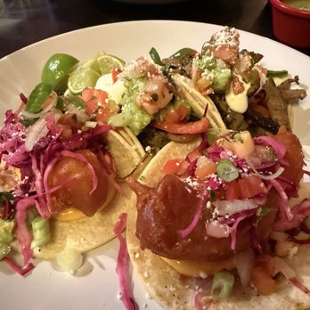 Fonda Garibaldi - Fish Tempura Fish - Two tacos filled with fried fish, topped with shredded vegetables, guacamole, and sauces, served on a white plate. - New Mexican Cuisine Near Me - Brooklyn, New York