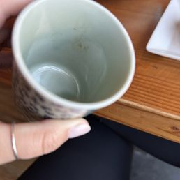 Dirty tea cup only one shown. Both were dirty - A person holds an empty ceramic mug with some stains inside, positioned over a wooden table with dishes and bowls nearby.