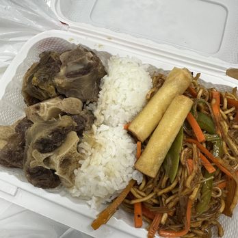 Chibogan - Oxtail Combo Meal - A foam takeout box contains oxtail, white rice, two spring rolls, and stir-fried noodles with carrots and green beans. - Filipino Near Me - Mount Prospect, Illinois