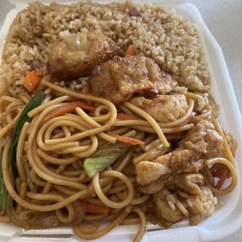 Asian  Cafe - Chicken Lo Mein lunch plate - A foam takeout container holds a meal consisting of chicken pieces with gravy, a portion of fried rice, and lo mein noodles mixed with vegetables such as carrots and green onions. The meal appears to be a typical Chinese takeout dish, served in a disposable container. - Chinese Near Me - Eagle  Mountain, Utah
