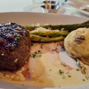 Dauphin's - My Filet - A plated meal includes a cooked filet mignon steak with grill marks, a side of grilled asparagus spears, and a scoop of mashed potatoes with gravy. The dish is presented on a white plate, with some sauce and herbs visible, suggesting a fine dining setting. - Seafood Near Me - Mobile, Alabama