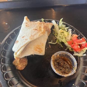 Taco Cabana - Bean and Cheese Burrito - A bean and cheese burrito is on a black plastic plate, accompanied by shredded lettuce, diced tomatoes, and salsa in a small cup. - Mexican Near Me - Albuquerque, New Mexico
