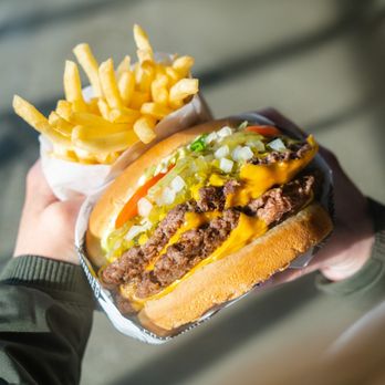 Fatburger - a hand holding a hamburger and french fries - Burgers Near Me - Los Angeles, California Fatburger - a hand holding a hamburger and french fries - Burgers Near Me - Los Angeles, California