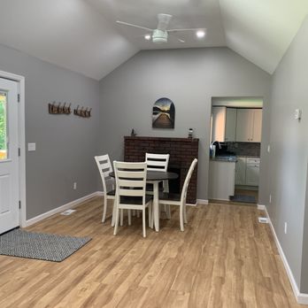 Build Right 518 - A dining space features a round table with white chairs, a brick fireplace, and a view into the kitchen with white cabinets. - General Contractors Near Me