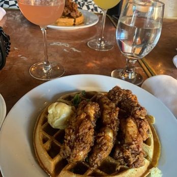Herbie's Restaurant - A dish of fried chicken on a waffle with butter is served on a white plate, with glasses of rosé, white wine, and water on the table. - New American Near Me - Clayton, Missouri