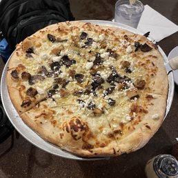 Tommy Boy Pizza - A large pizza with cheese, mushrooms, and crumbled cheese toppings on a round tray, with a glass of water and lemon in the background.