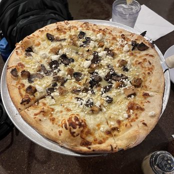 Fire Slice Pizzeria - Tommy Boy Pie - Small 12" - A large pizza with cheese, mushrooms, and crumbled cheese toppings on a round tray, with a glass of water and lemon in the background. - Pizza Near Me - Amarillo, Texas
