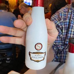 My husband loved the individual little bottles of spumante. - A person holds a small, white bottle of Moletto Dolce Amore wine in a restaurant with other diners and a TV screen in the background.
