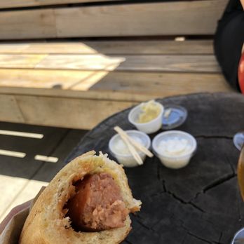 Bratzermann - Smoked brat in their easy-to-eat roll/bread thing with onions and sauerkraut in the background - Food Trucks Near Me - Costa Mesa, California Bratzermann - Smoked brat in their easy-to-eat roll/bread thing with onions and sauerkraut in the background - Food Trucks Near Me - Costa Mesa, California