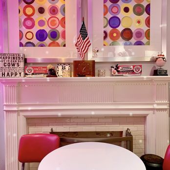 Moo Moo Cows - Seating area inside - The image shows the inside of Moo Moo Cows, an ice cream shop, with pink lighting, colorful circular artwork on the wall, and a white fireplace mantel with decorations. - Ice Cream & Frozen Yogurt Near Me - Baltimore, Maryland
