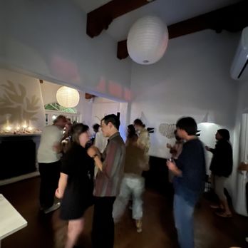 La Reina - Hey Kiddo! DJ dance party - A group of people are gathered in a dimly lit room, dancing and talking, with paper lanterns hanging from the ceiling. - Bars Near Me - Santa Fe, New Mexico