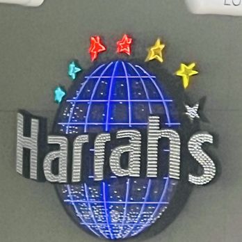 The Pomp - The image shows a decorative sign featuring the word 'Harat's' in large, illuminated letters with a globe design behind it. The sign is decorated with neon lights in blue, and there are star-shaped lights in red, yellow, and blue above the globe. The sign appears to be mounted on an indoor wall, with ceiling fixtures visible at the top of the image. - Shopping Centers Near Me - Pompano Beach, Florida
