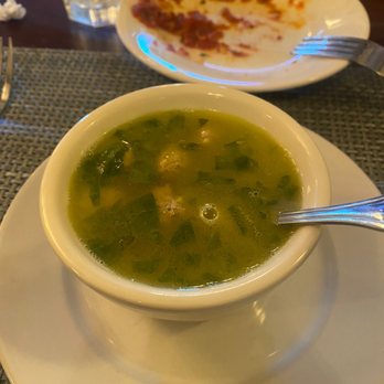 Bucci's - Wedding - A bowl of green soup with a spoon, placed on a white plate, with a partially eaten pizza on a plate behind it. The setting appears to be a restaurant. - Italian Near Me - Rocky River, Ohio