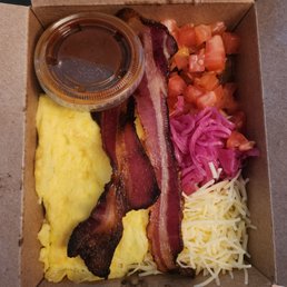 breakfast bowl with salsa, bacon, scrambled eggs, shredded cheese, chopped tomato, and pickled onions. black beans and potatoes as base.