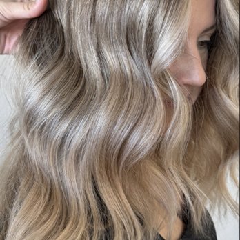Arrow & Mane - A woman with long, blonde, wavy hair is captured in a profile view, showing her hair's texture and color, with a neutral background. - Hair Extensions Near Me - Tracy, California