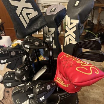 PXG Denver - My pxg equipment w Scotty putter - A golf bag contains various clubs with PXG and Titleist headcovers, including a red one, set indoors with household furniture in the background. - Golf Equipment Near Me - Centennial, Colorado