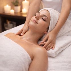 Perfect Touch Therapeutic Massage - Woman lying on a massage table * Towel wrap * Therapist hands on neck * Candles in background * Soft lighting