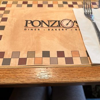 Ponzio's - A Ponzio's restaurant placemat with a logo, a fork on a napkin, and a wooden table surface. - Bakeries Near Me - Cherry Hill, New Jersey