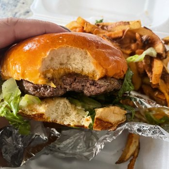 Earl's BBQ - Prime Cheese Burger - A partially eaten cheeseburger with lettuce, cheese, and a shiny bun, held in hand, with fries and roasted vegetables on a tray in the background. - Donuts Near Me - Chicago, Illinois