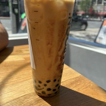 Teaspoon - Berkeley - Black Sugar Assam - A tall plastic cup of bubble tea with black tapioca pearls at the bottom, sitting on a wooden table near a window with sunlight. - Bubble Tea Near Me - Berkeley, California
