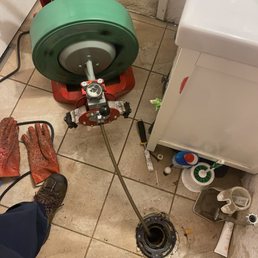 The photo is of a bathroom floor with a snake down the drain where a toilet normally sits. The photo is of a bathroom floor with a snake down the drain where a toilet normally sits.