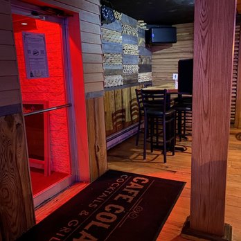 Cafe Colao - Main Entrance door from inside, high table seating - The photo depicts the interior of Cafe Colao, featuring a red-lit entrance door, wooden wall decor, and a seating area with high tables and chairs. - Dominican Near Me - Hazleton, Pennsylvania