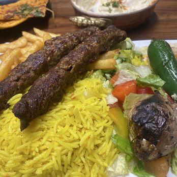 Aleppo Kebab - Aleppo Kebab Meal - A meal featuring two grilled kebabs on yellow rice, accompanied by salad, a green chili pepper, and side dishes including hummus and a vegetable omelette. - Salad Near Me - Ajax, Ontario