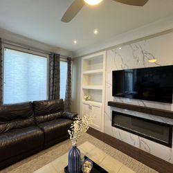 Kimmberly Capone Interior Design - Sophisticated living space featuring twin curved sofas, textured stone fireplace, and built-in illuminated shelves with modern décor.