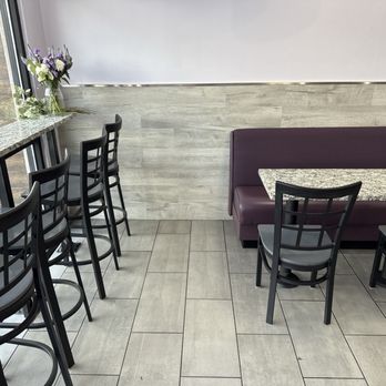 Donut Mart Cafe - Seating - A dining area features a row of black bar-height chairs along a window with flower arrangements, and a booth with a granite table against a light wood-paneled wall. - Donuts Near Me - Albuquerque, New Mexico