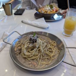 Truffled Mushroom Spaghetti - A dish of mushroom spaghetti with creamy sauce, grated cheese, and a garnish, served on a metal plate at a restaurant table.