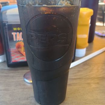 Laguna Burger - Pepsi products are a plus in my book. - A tall, cylindrical glass with the Pepsi logo embossed on it is filled with a dark beverage, likely soda, and ice. The glass is on a wooden table in a casual restaurant setting, with condiments and a menu visible in the background. - Burgers Near Me - Albuquerque, New Mexico