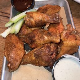 Smoked chicken wings - Fried chicken wings served on a metal tray with celery sticks, a small cup of dark sauce, and a cup of ranch dressing, on a wooden table.