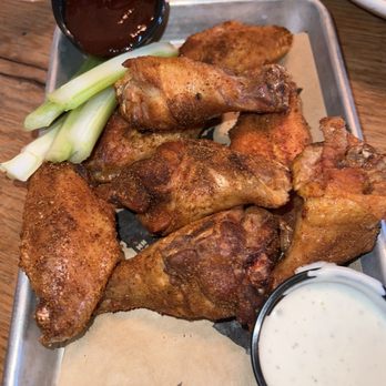 Revolve Hall - Smoked chicken wings - Fried chicken wings served on a metal tray with celery sticks, a small cup of dark sauce, and a cup of ranch dressing, on a wooden table. - Tacos Near Me - Apple Valley, Minnesota