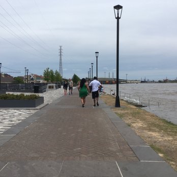 The Moon Walk - Cement seated steps by the river in the distance and salt and pepper brick expansion deck area - Parks Near Me - New Orleans, Louisiana The Moon Walk - Cement seated steps by the river in the distance and salt and pepper brick expansion deck area - Parks Near Me - New Orleans, Louisiana