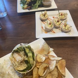 Wasabi Deviled Eggs - The image shows a wooden table with a salad, deviled eggs, and a wrap with potato chips, likely at a restaurant or cafe setting.