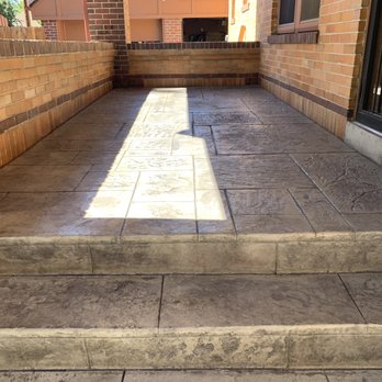 Gumer Concrete LLC - A concrete patio with two steps is bordered by brick walls and attached to a brick building with a door and window. - Masonry/Concrete Near Me - Denver, Colorado