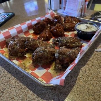 Catman Cafe - A metal tray holds chicken wings with sauce, accompanied by a small container of dipping sauce, on a restaurant counter with condiments and menus. - American Near Me - Mansfield, Massachusetts